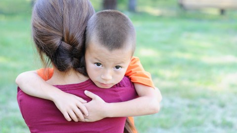 A young child hugging his mother and exhibiting strong signs of anxiety.