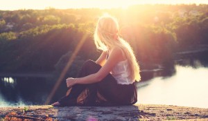 Woman with ADHD sitting on top of mountain overlooking lake at sunset thinking about her diagnosis