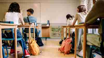 Students sit at desks and face the front of a classroom.