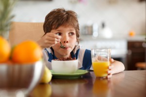 Cute boy with ADHD drinking orange juice and eating muesli for breakfast