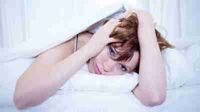 Woman with ADHD in bed, unable to sleep and holding head, with frustrated expression
